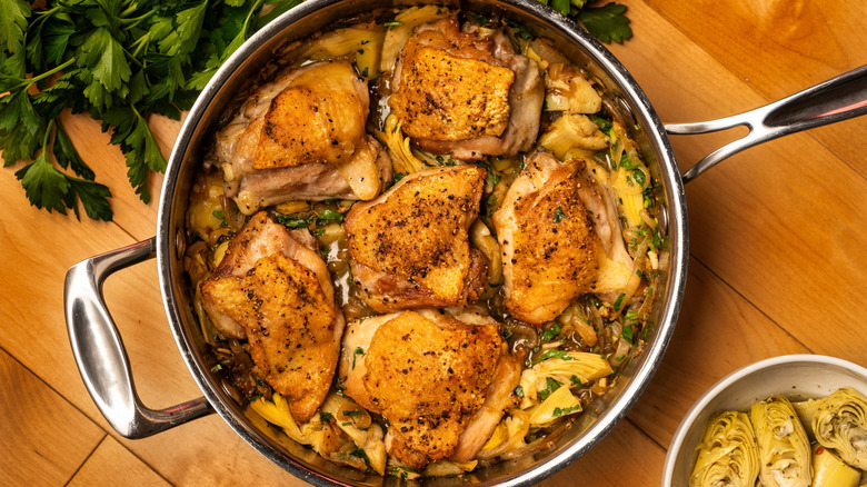 Chicken thigh pieces in a pan with artichokes