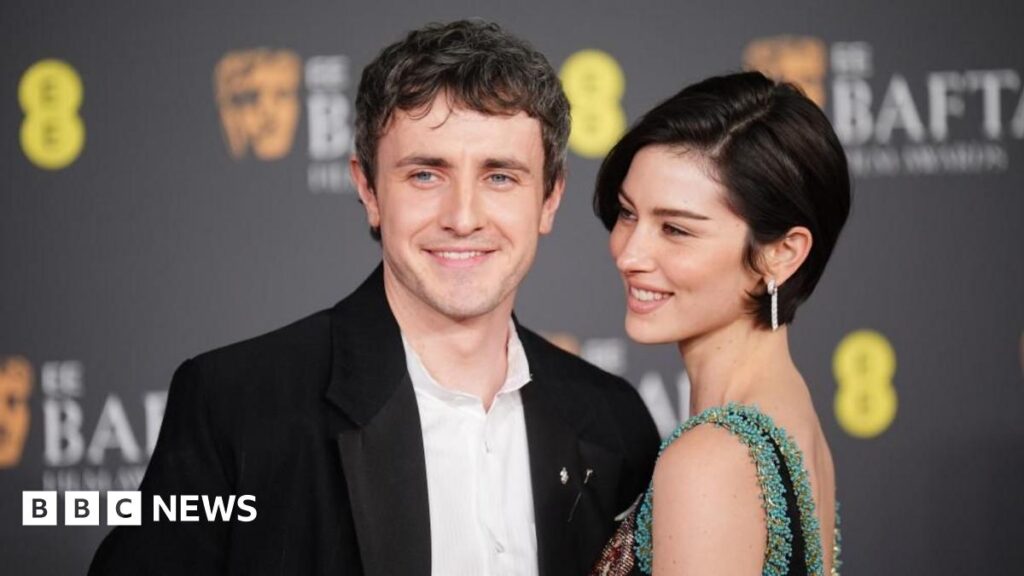 Six backstage highlights from the Bafta Film Awards A woman with black hair with a white head band on stares directly into the camera. She has long eyelashes and a brown top on. She is sat on a chair which has images of guinea pigs printed on it.