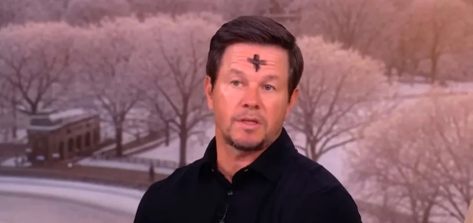 A person with a black cross on their forehead is speaking against a snowy landscape background