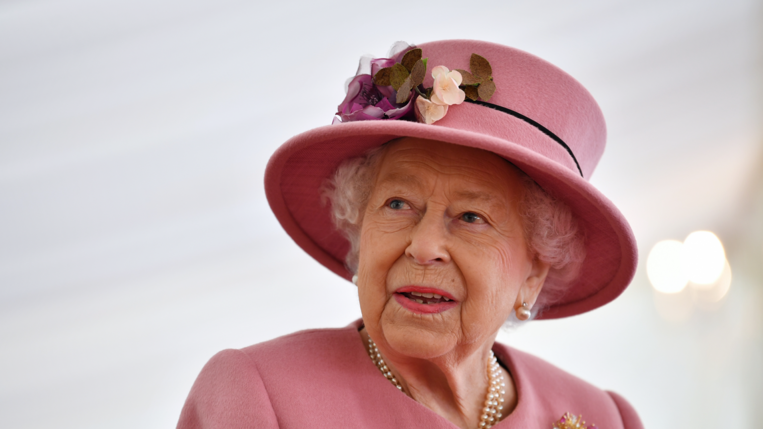Queen Elizabeth wearing a pink hat and coat looking to the side