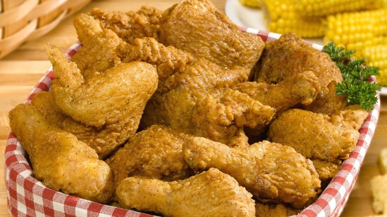 A platter of fried chicken, with corn on the cob in the background.