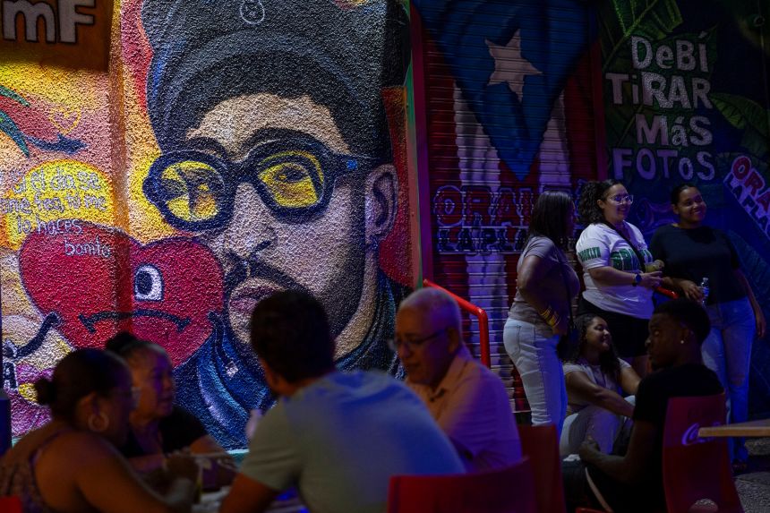 People sit in front of a mural of Puerto Rican singer Bad Bunny at La Placita de Santurce in San Juan, Puerto Rico on July 12, 2025.