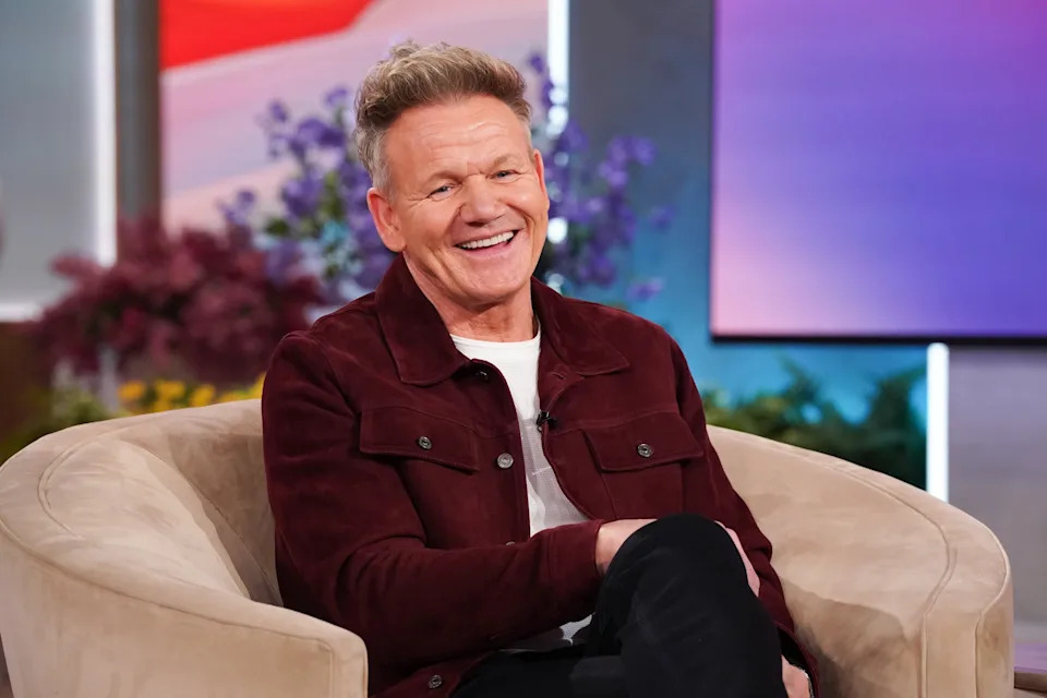 Celebrity sits on a talk show set, smiling in a casual outfit with a jacket and T-shirt
