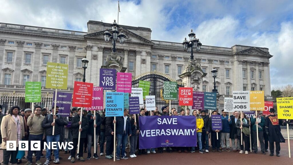 A large group of protesters outside Buckingham Palace, with multiple coloured placards saying "keep calm and curry on", "many customers are heartbroken", "stop the greedy crown estates from evicting Veeraswamy".
