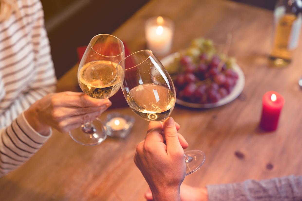 Two hands clinking glasses of wine over a romantic dinner.