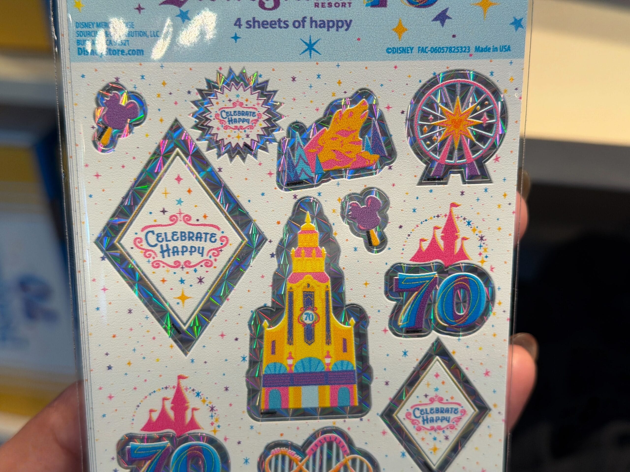 The stickers on the visible sheet feature holographic edges and designs like the 70th anniversary logo, churros, Mickey ice cream bars, 