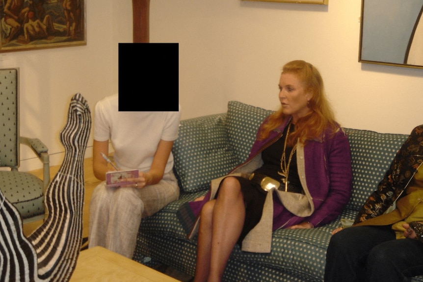 A woman sitting on a sofa looking on. Next to her, another woman is sitting, but her face has been redacted.