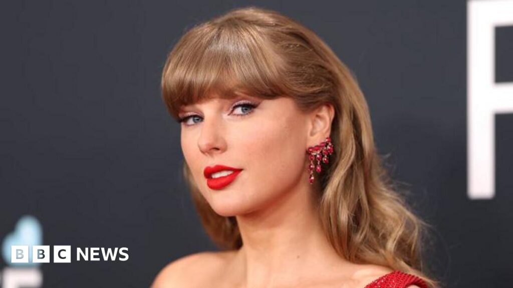 Taylor Swift, wearing a red dress, smiles for the camera during the Grammy Awards ceremony