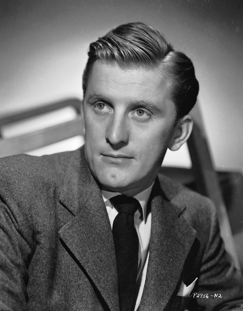 Kirk Douglas gazes away from the camera in a suit and black tie.