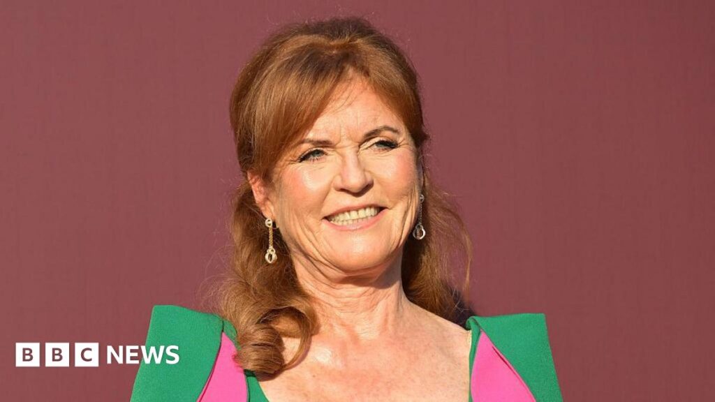 Sarah Ferguson wrote ‘marry me’ to Epstein, latest files show Sarah Ferguson stood in front of a dark red back drop. She is wearing a green dress with pink parts to it.