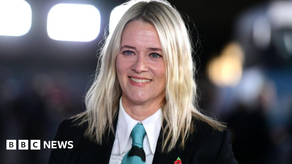 Edith Bowman ‘heartbroken’ after case with ashes goes missing Edith Bowman is wearing a black suit jacket, a white shirt and a blue tie. She is smiling, with blurred bright lights behind her.
