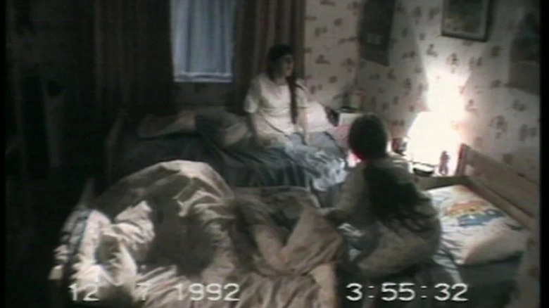 Michelle Wesson as Suzanne and Cherise Wesson as Kim sitting in their beds looking at something illuminated by a small lamp on the wall behind their beds in Ghostwatch