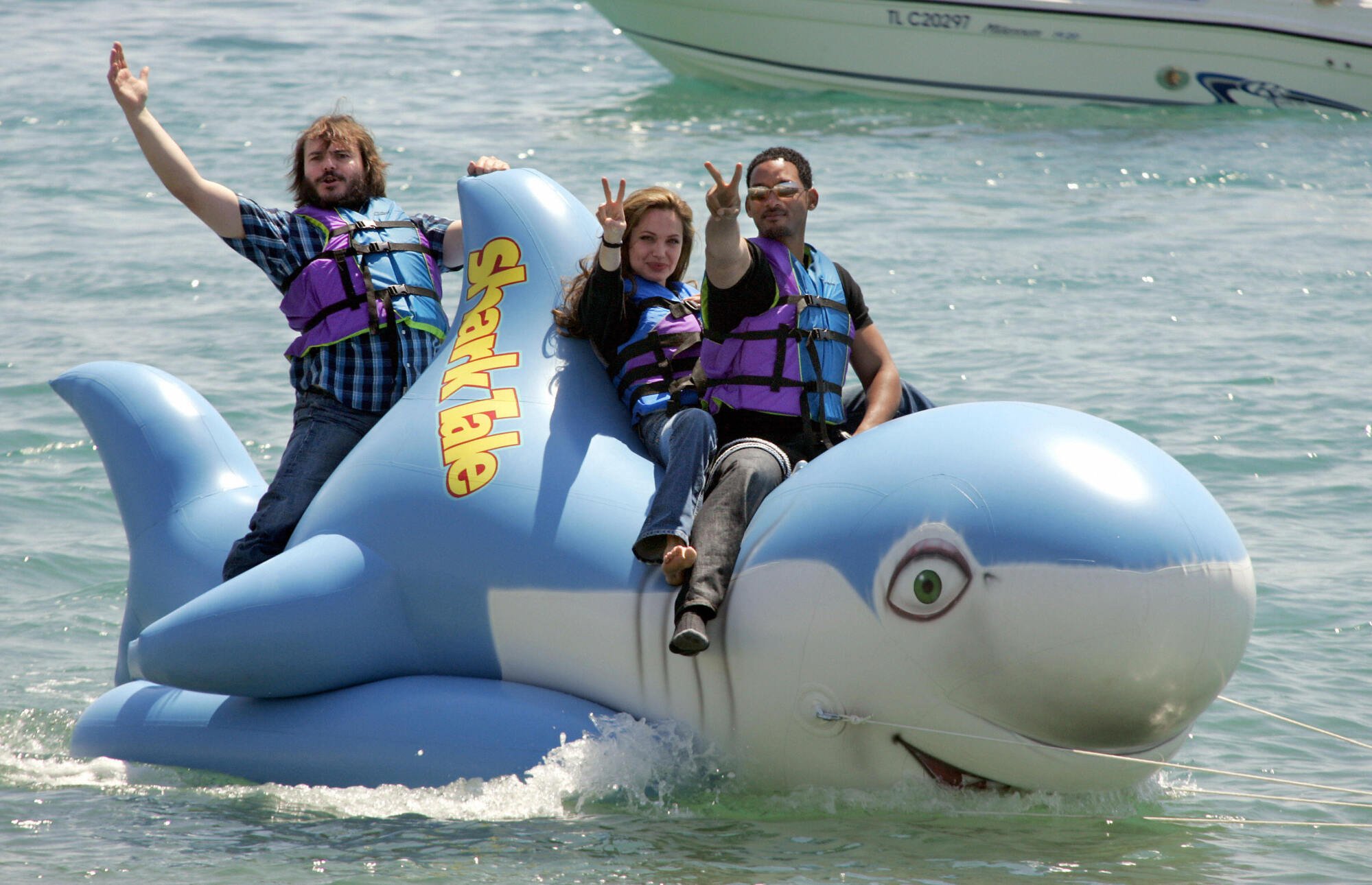 Three people sitting on a inflatable shark in the ocean.