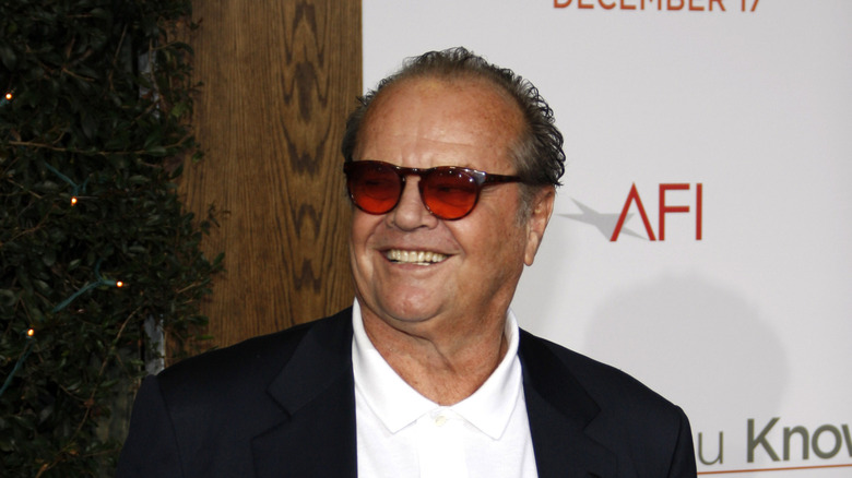 Headshot of Jack Nicholson wearing white shirt with black jacket and red glasses