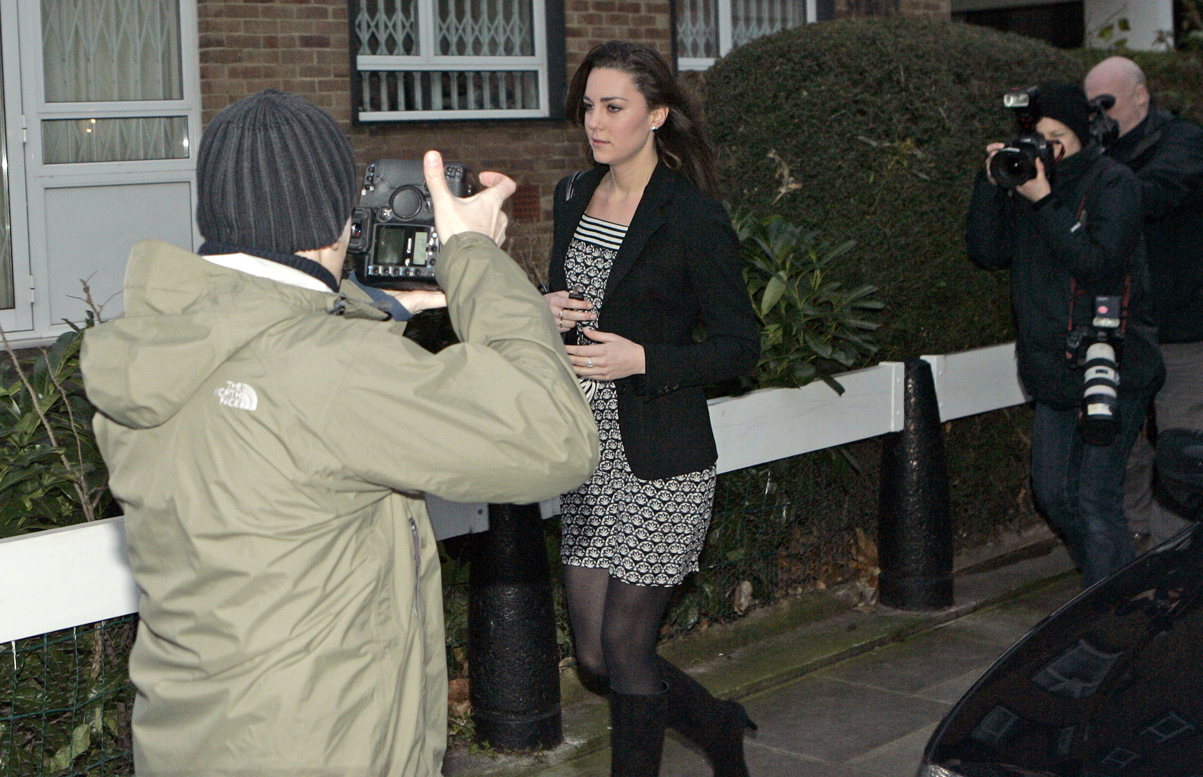 Kate Middleton walking down a street in a black dress and being hounded by paparazzi