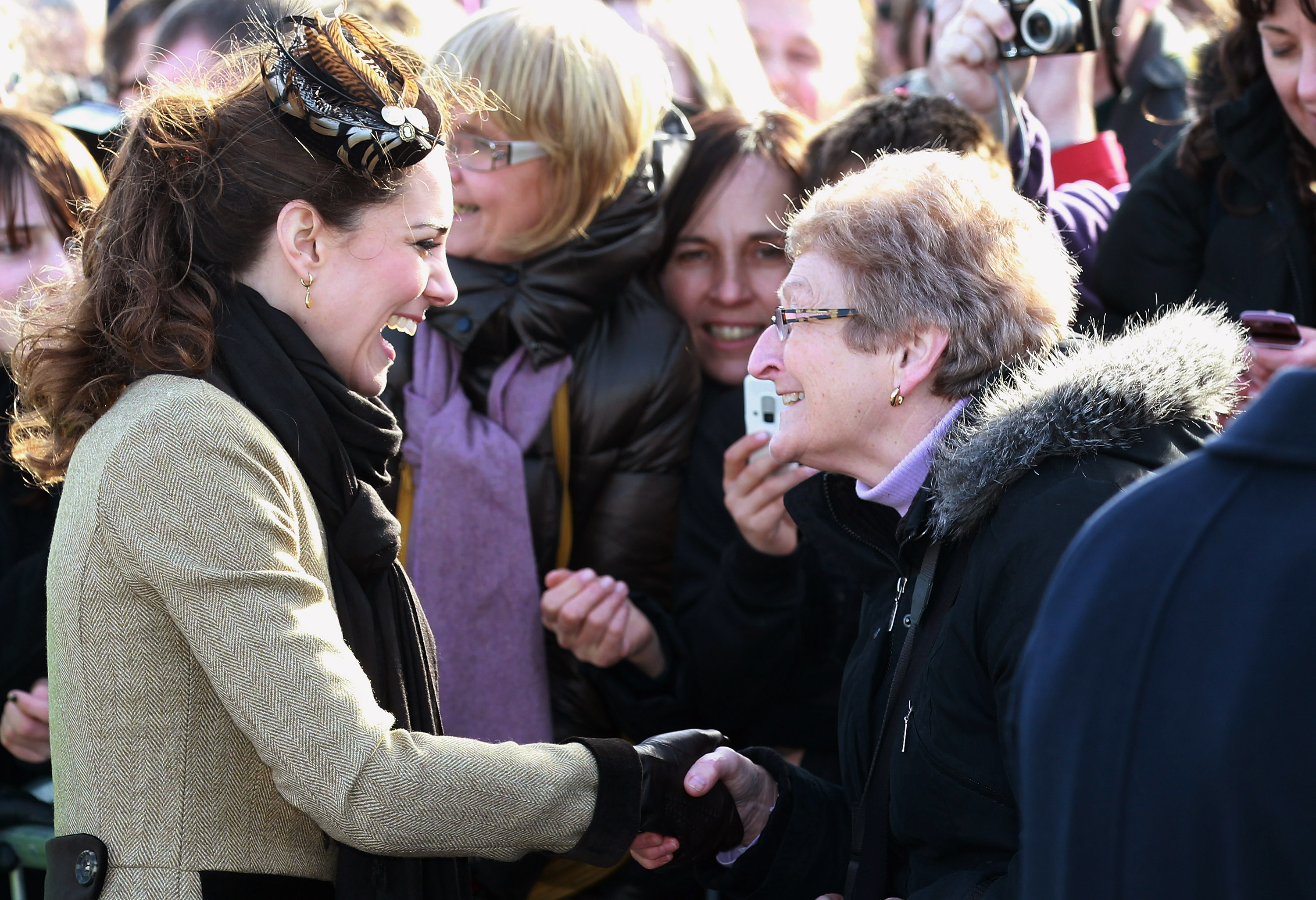 Kate Middleton wearing a brown coat shaking hands with an elderly woman in 2011