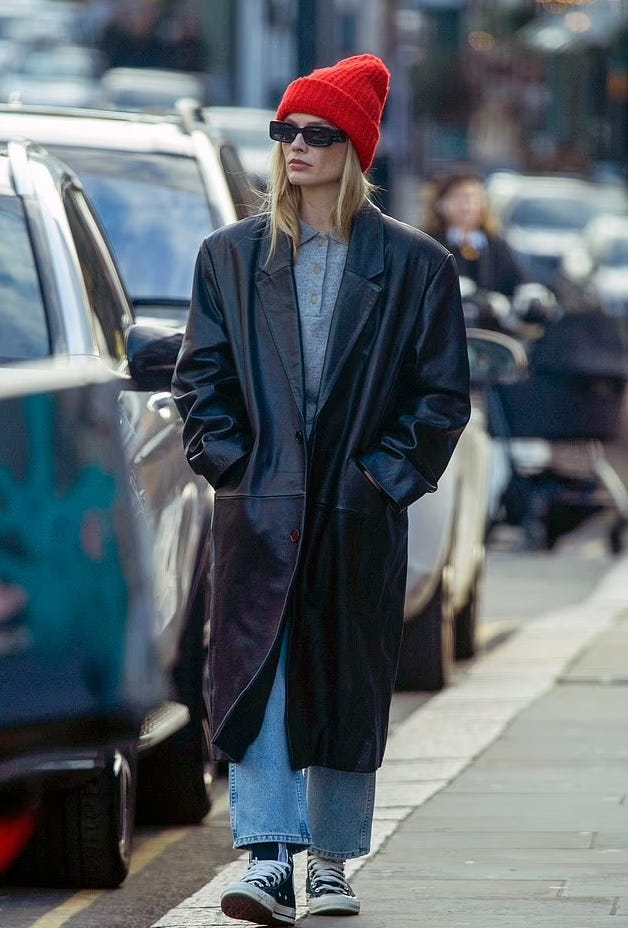 individual walking in urban setting wearing a long black coat and red beanie