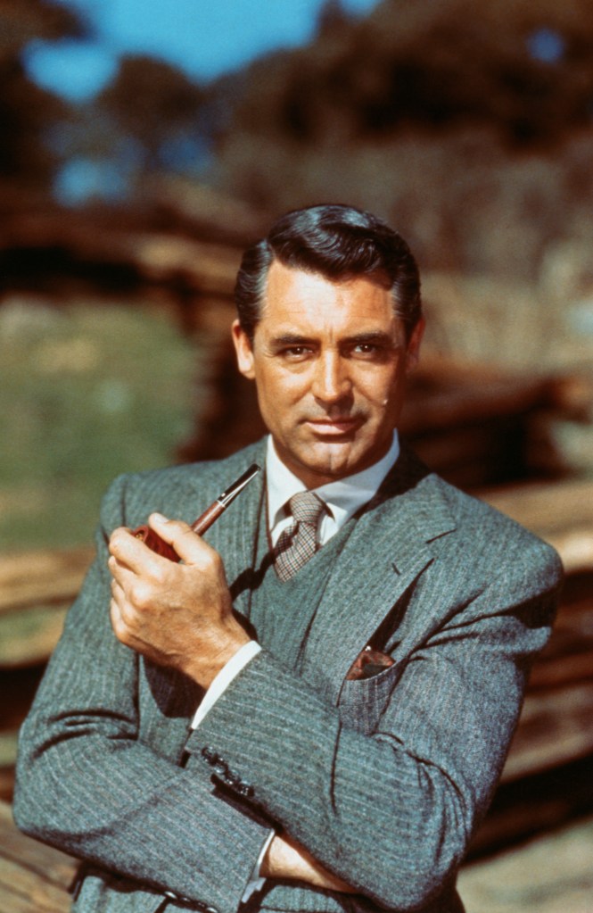 Cary Grant, a mid-adult man in a gray pinstripe suit, white shirt, and patterned tie, holds a pipe in his right hand.