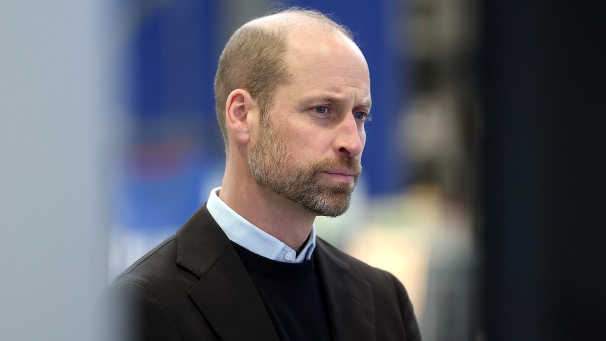 Prince William sitting and listening to scientists while surrounded by computer hardware and monitors.