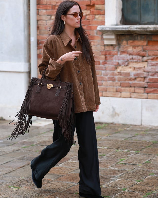 a person walking in a brown corduroy shirt and black pants carrying a fringed handbag