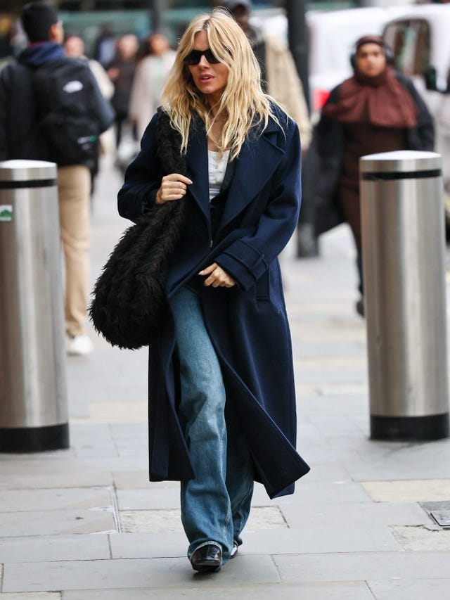 woman walking on a city street wearing a long coat and carrying a bag