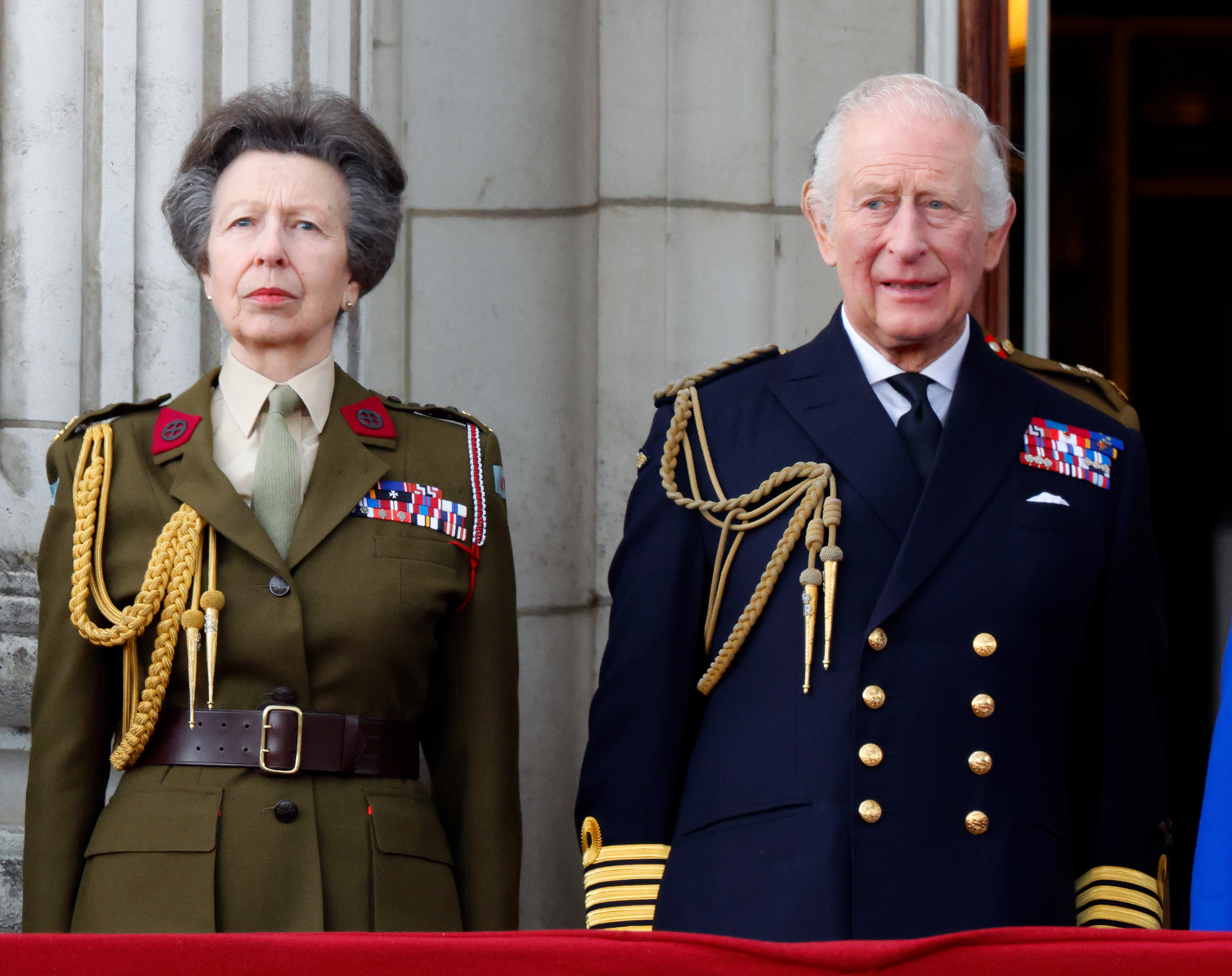 Princess Anne and King Charles standing on the palace balcony wearing uniforms