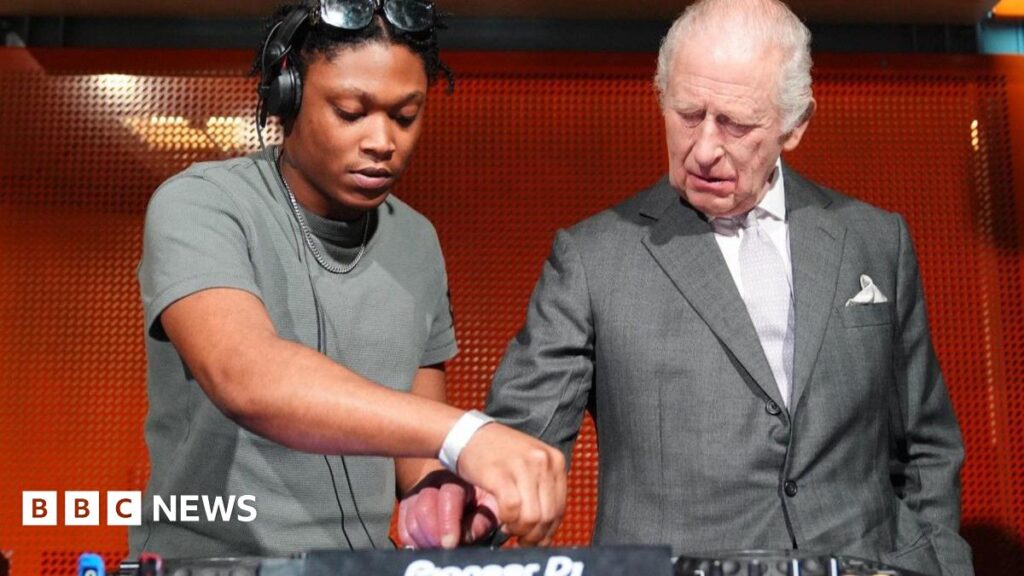 King Charles hits the DJ decks during Manchester arts venue visit Christian St Louis helps King Charles operate his DJ deck during a visit to Aviva Studios in Manchester, the home of Factory International. Charles is wearing a light grey suit with a white shirt and a pale grey tie.