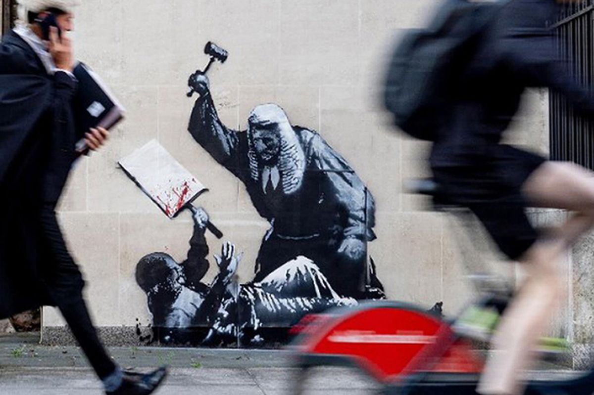 A photo of people walking past a Banksy artwork