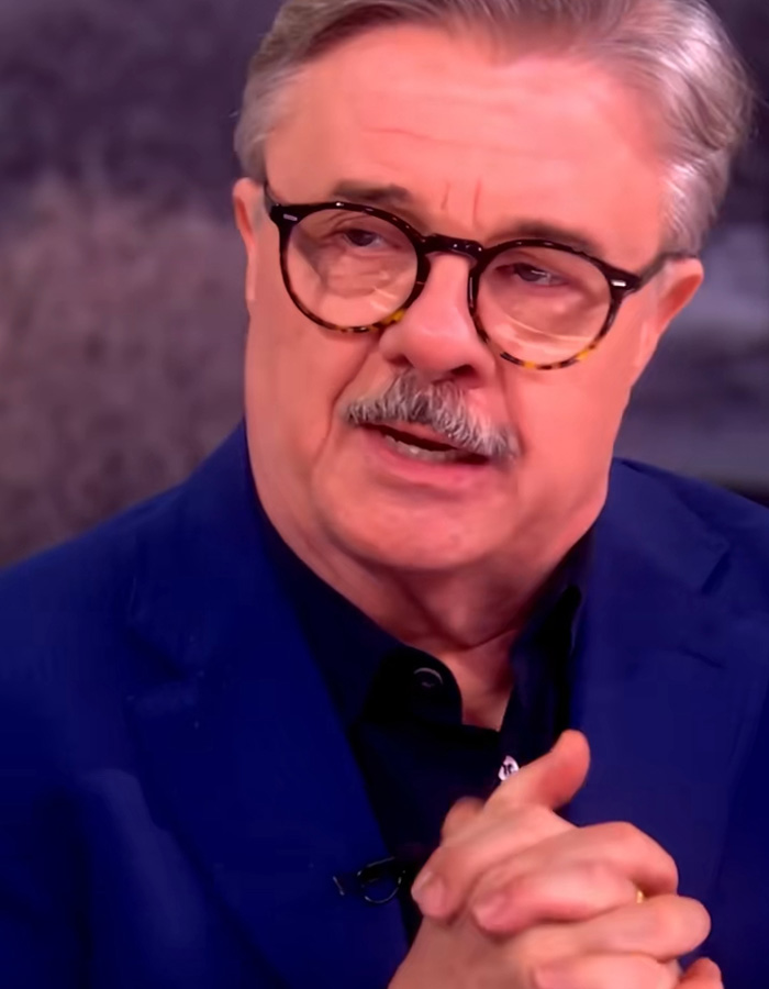 Older man with glasses in a navy jacket discussing Timothée Chalamet as a sage ahead of the Oscars in an interview setting.