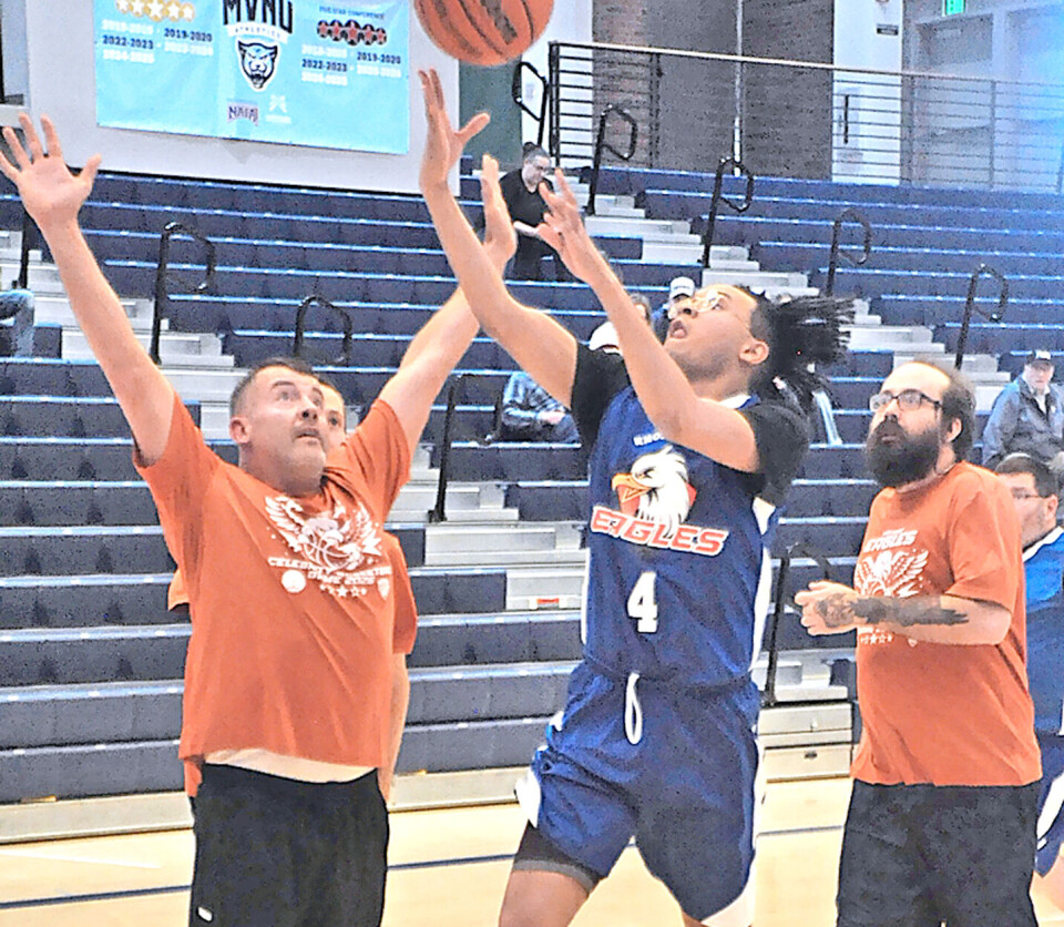 A basketball player in blue shoots as an opponent in orange tries to block.