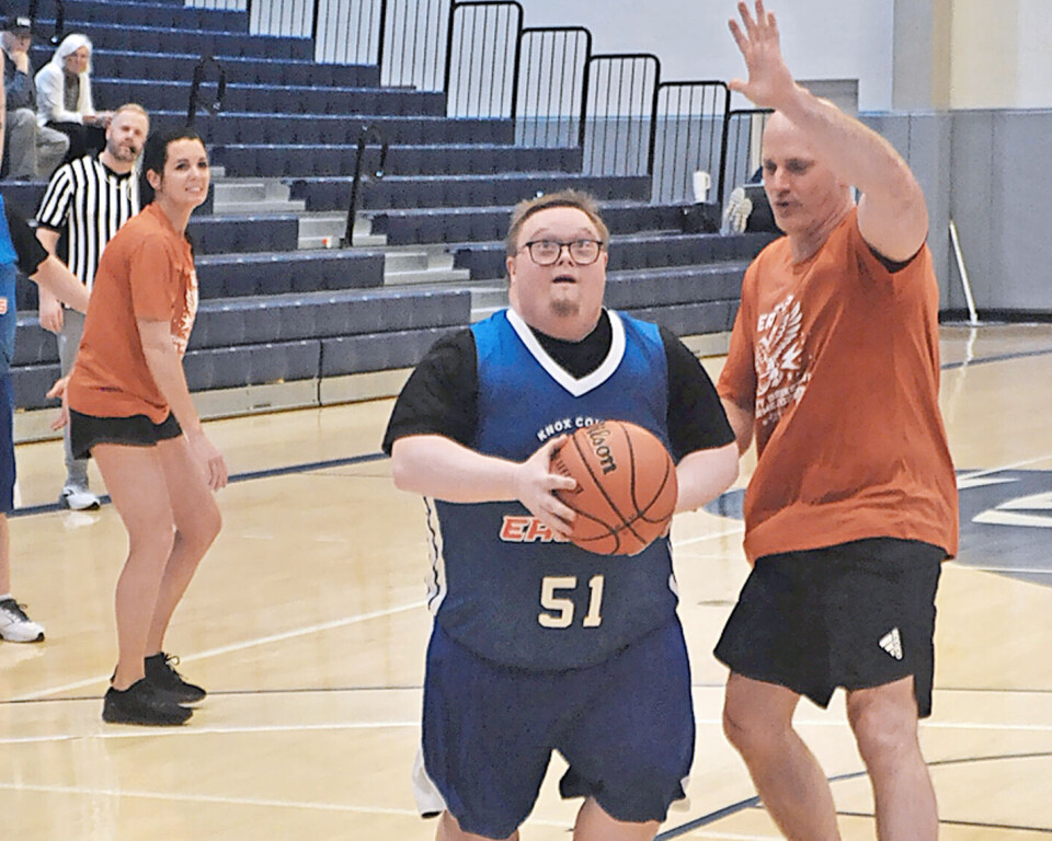 A player with a basketball is defended in a gym setting.