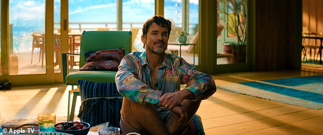 Bomer sits on a wood floor at a beach house