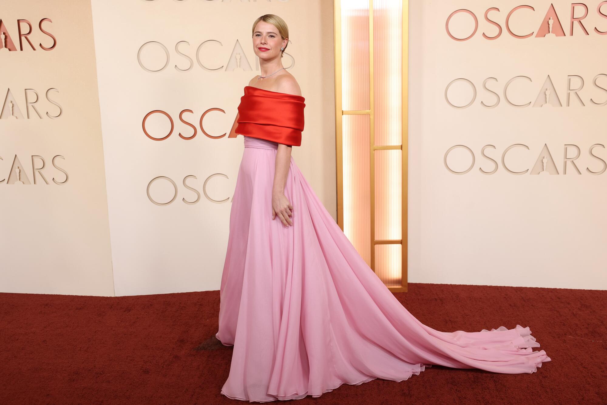 Jessie Buckley, wearing a red and pink gown, poses on the red carpet. 