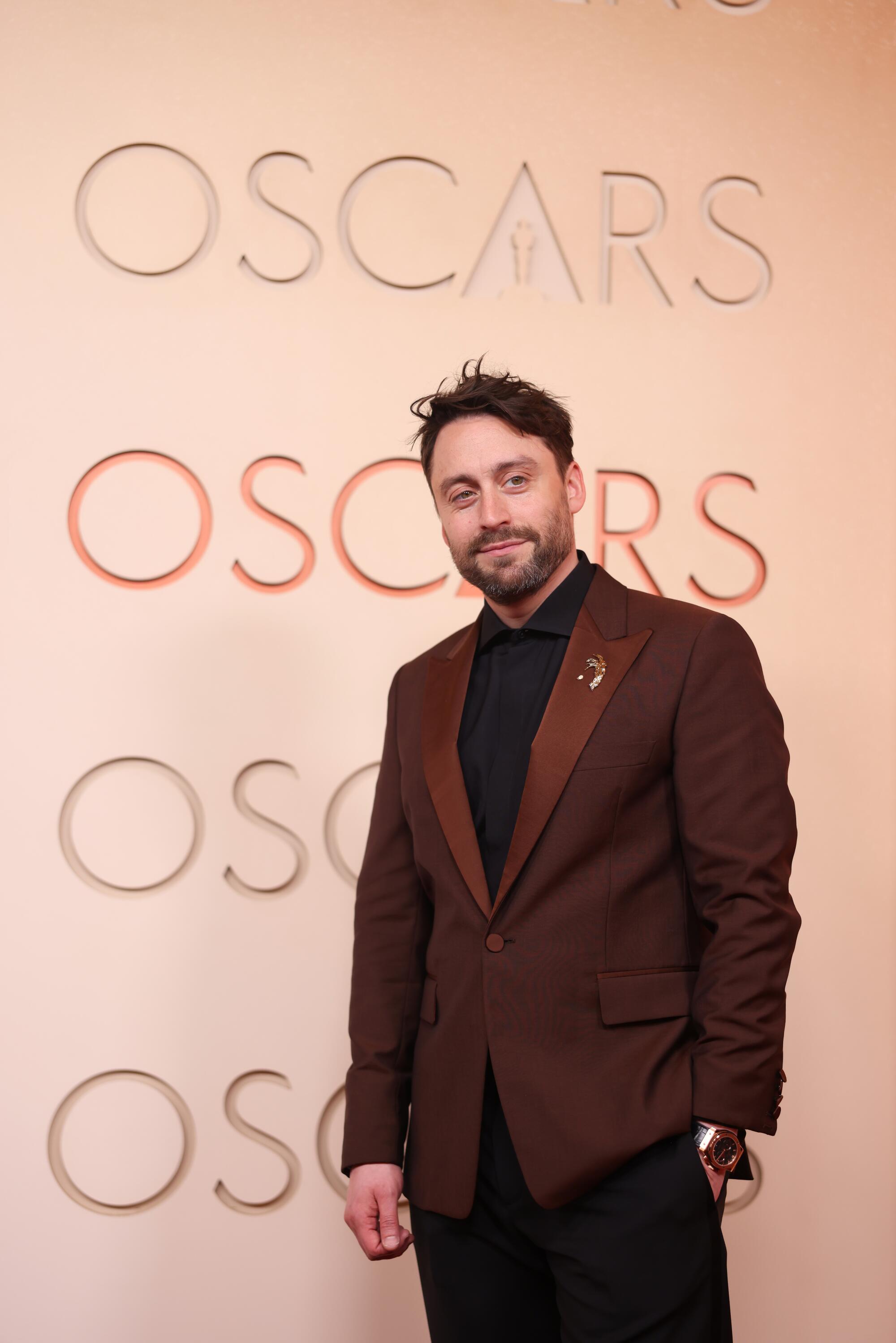 Kieran Culkin, wearing a brown blazer, poses on the red carpet.