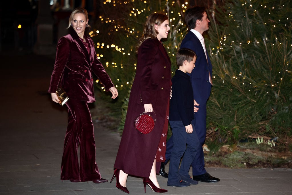Four people walk in front of a giant tree displaying white lights.