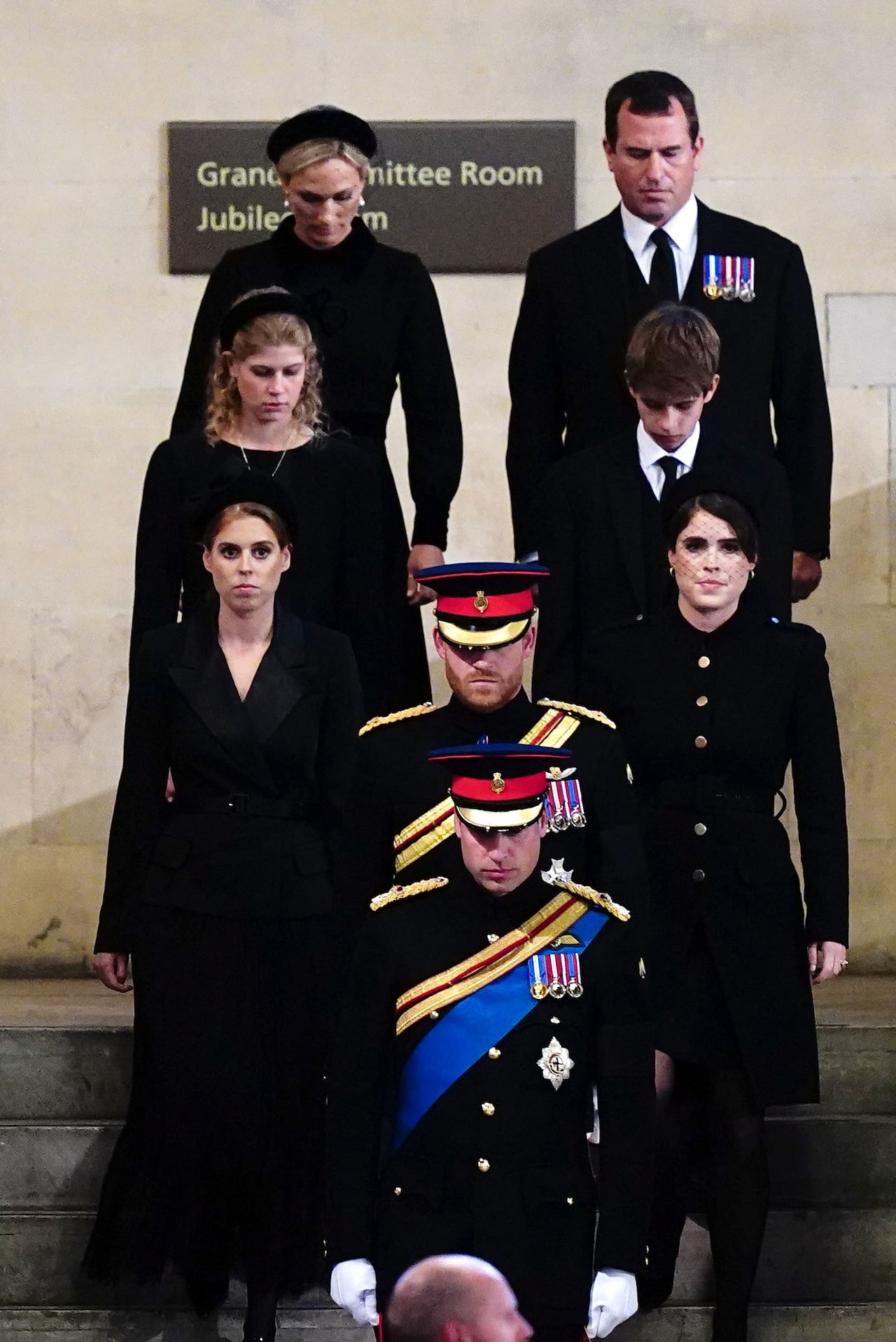 Eight people dressed in black walk down a set of stairs.