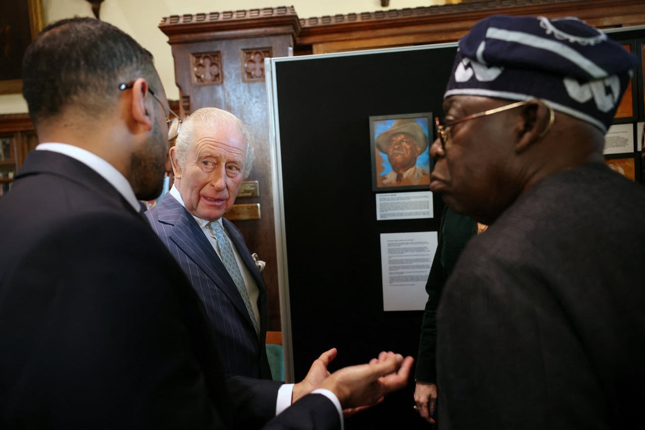 Three people talk with one another in front of a painting.