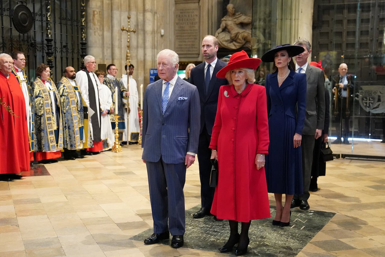 A group of people stand inside the entrance of a large abbey, with a group of clergy standing along a nearby wall.