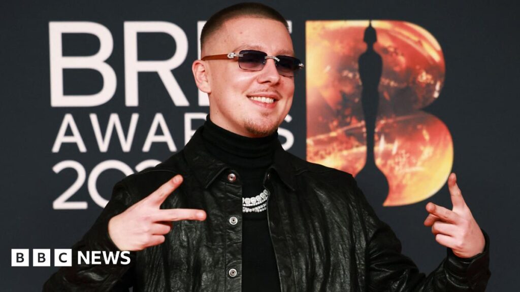 Manchester rapper Aitch to star in Mobo Awards Aitch, with short brown and dark shades wearing a dark polo neck swearer and black leather jacket poses on the red carpet during the BRIT Awards at the Co-op Live Arena, in Manchester, Britain, 28 February 2026.