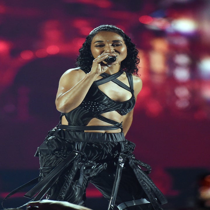 Chilli performing on stage wearing a strappy, edgy outfit with metallic accents, holding a microphone