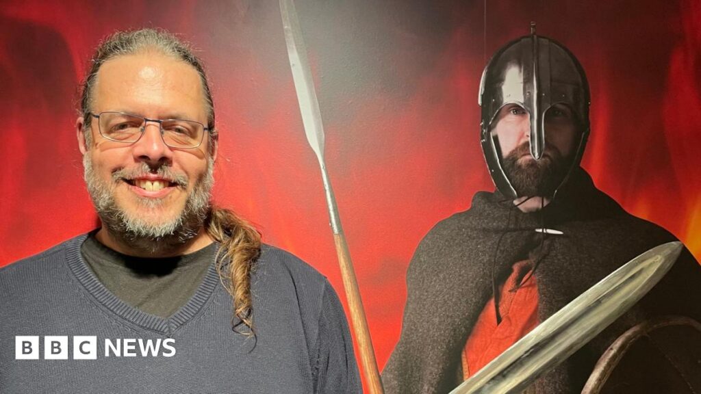 A glass conical drinking beaker lying on its side with its wide rim on the left narrowing to the right. It is decorated in fine evenly spaced lines of flace. It still has mud clinging to it. Found at Wendover.