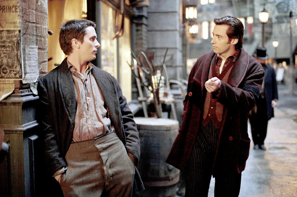 Two men in Victorian-era attire exchange intense glances in a cobblestone street, suggesting tension or a significant discussion in a period drama