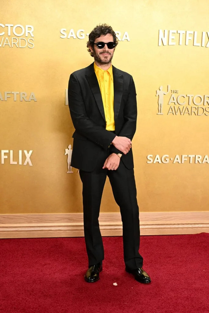 Adam Brody Prada Actor Awards 2026, black Prada suit yellow silk shirt, Adam Brody red carpet style, Cartier Tank à Guichets, statement menswear, bold shirt styling, contemporary tailoring