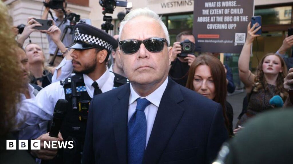Huw Edwards, wearing a suit and sunglasses, outside court, surrounded by media and protestors
