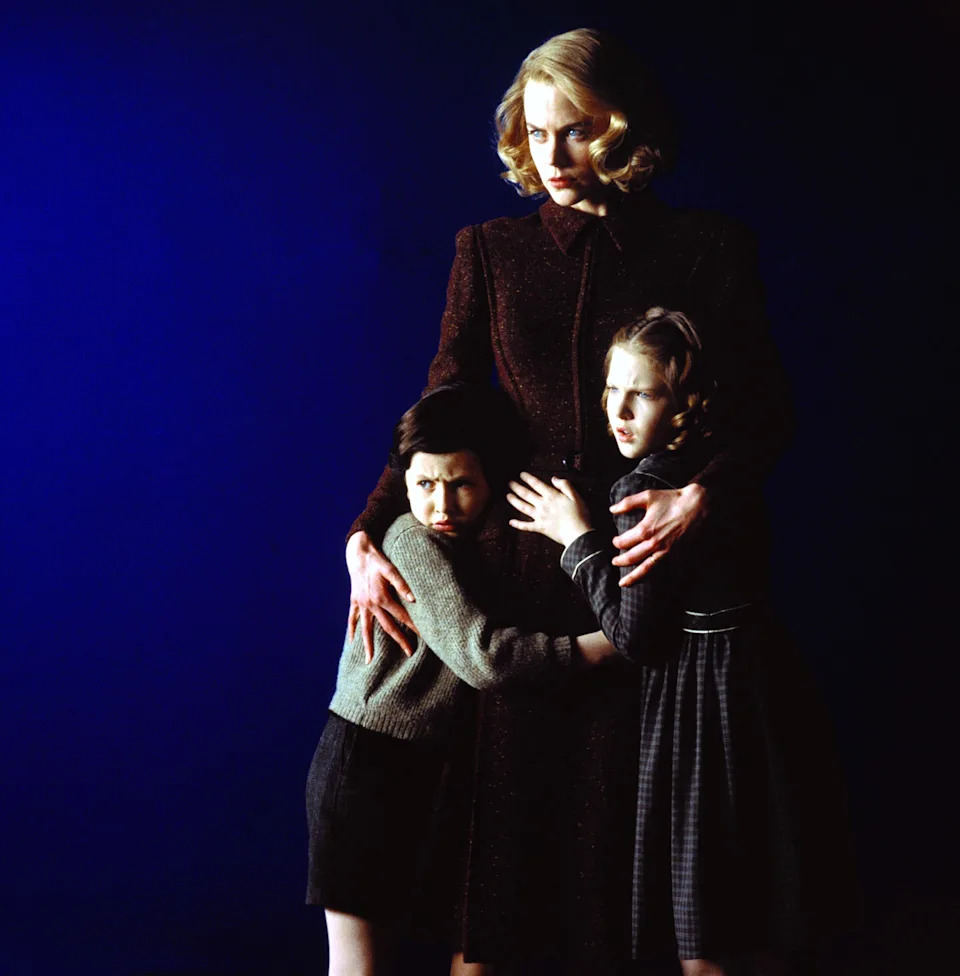 A woman in vintage-style clothing holds two children close, appearing protective