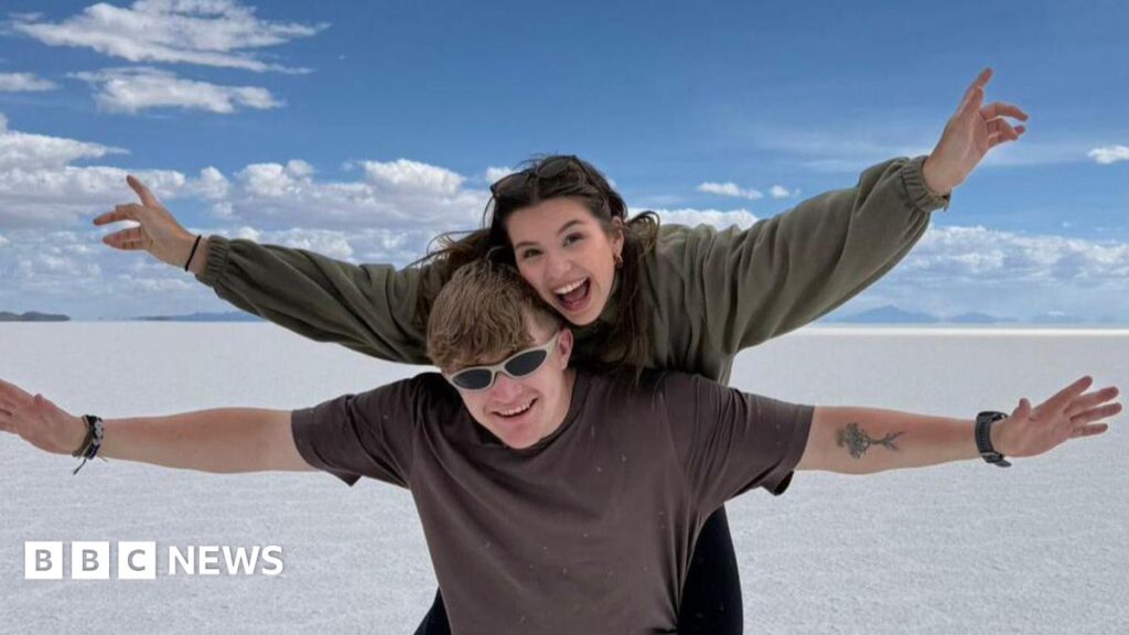 Cathie and Tricia pictured holding a glass of champagne each. They are both smiling. Tricia has her arm around Cathie.
