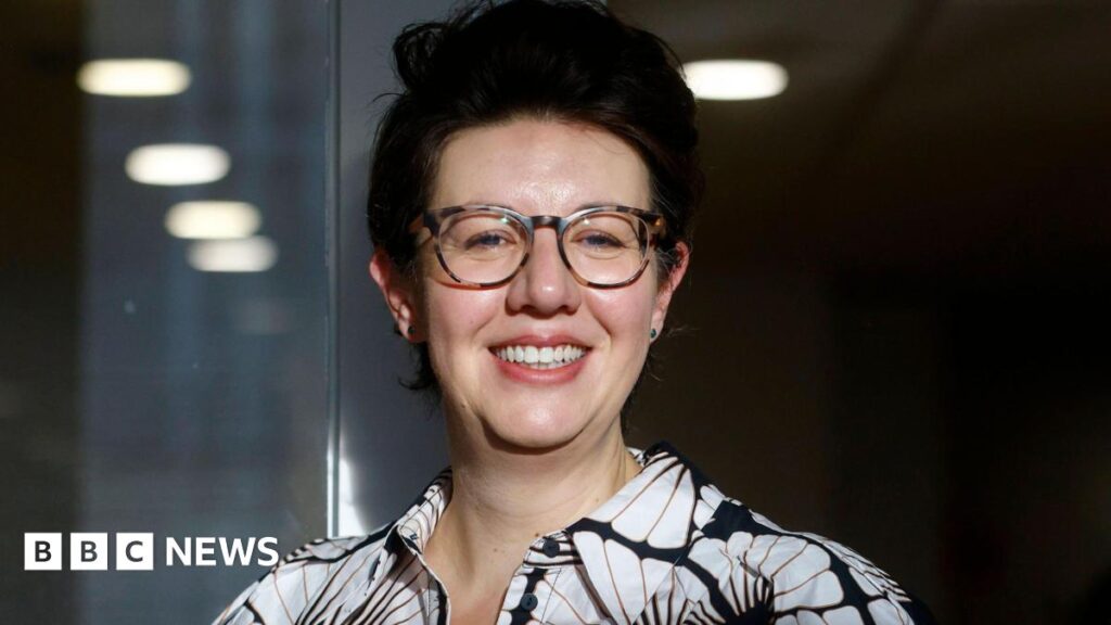 Nero Book Prize: Claire Lynch wins for debut novel inspired by real family separations Claire Lynch smiling, wearing glasses and a black-and-white patterned shirt
