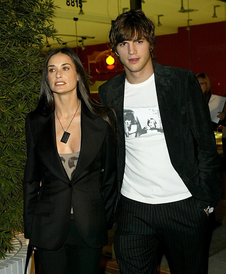 Two people walking side by side; one wearing a blazer and shirt, the other a jacket over a graphic tee with pinstriped pants