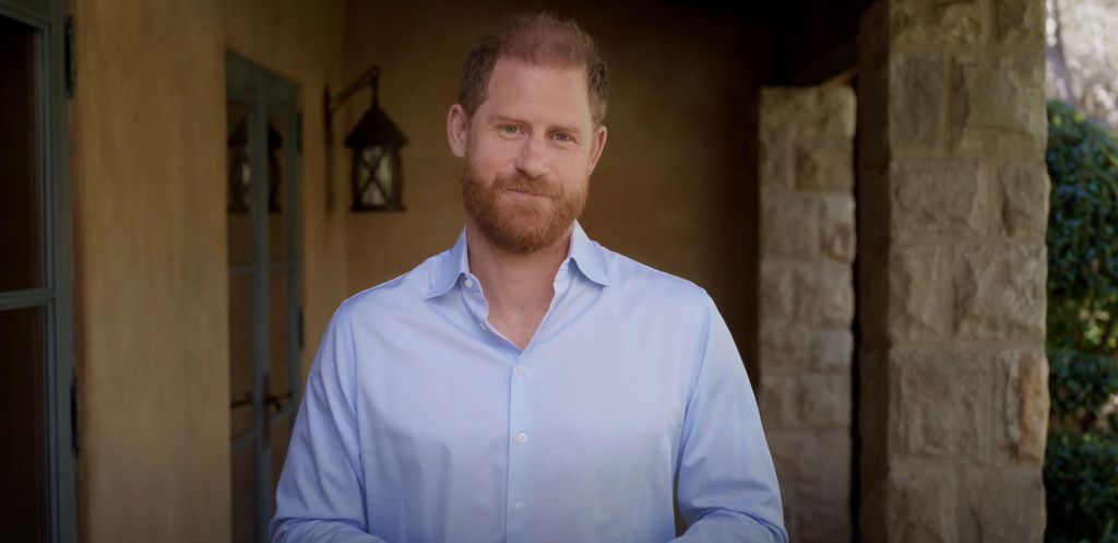 Prince Harry in a pale blue shirt standing outside his Montecito home
