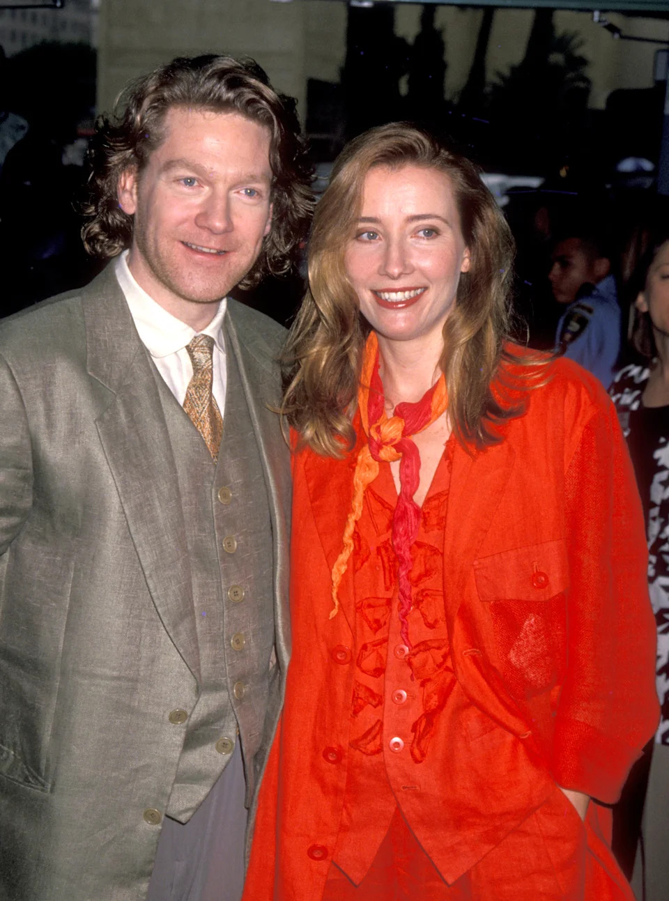 Two people smiling at an event, one wearing a suit and the other in a ruffled outfit with a matching scarf
